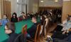 Młodzi ludzie siedzą przy długim stole nakrytym zielonym obrusem w sali konferencyjnej i słuchają wykładu.