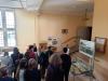 Młodzi ludzie stoją na holu głównym w Archiwum i oglądają wystawę na planszach oraz w szklanych gablotach.