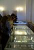 Ludzie zwiedzają wystawę w szklanych, oświetlonych gablotach wystawowych na sali wystawowej Archiwum.
