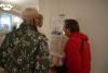 Trzy starsze kobiety przyglądają się planszy wystawowej z opisem miejscowości Wolimierz, zdjęciem i planami kościoła. Plansza stoi na sztaludze przy ścianie w wystawowej Archiwum.